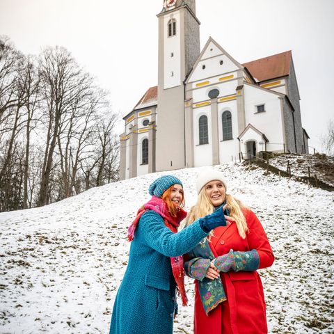 Ein Winterspaziergang zur Wallfahrtskirche St. Ottilia bei Biessenhofen... Zwei Frauen stehen vor der Wallfahrtskirche St. Ottilia in Biessenhofen, die Landschaft ist mit Schnee überzuckert.
