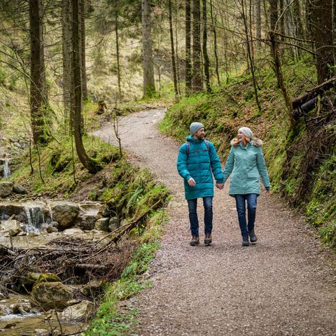 Wandern im Winter auf dem Wasserfallweg in Nesselwang Ein paar wandert entlang eines Bachs im winterlichen Wald ohne Schnee