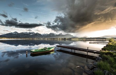 Sonnenuntergang am Hopfensee Blick auf den Hopfensee bei Füssen im Ostallgäu mit grünem Fischerboot beim Sonnenuntergang.
