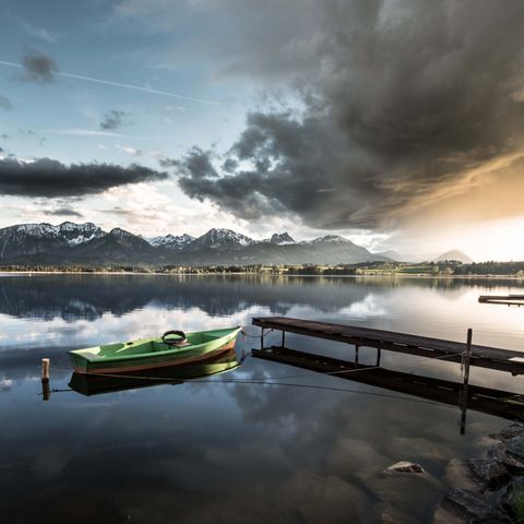 Sonnenuntergang am Hopfensee  Blick auf den Hopfensee bei Füssen im Ostallgäu mit grünem Fischerboot beim Sonnenuntergang.