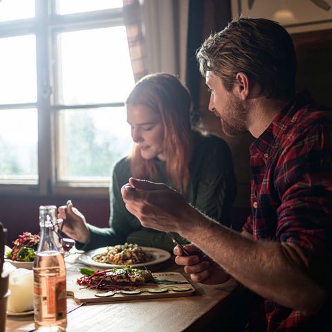 Eine gemütliche Einkehr in der Hündleskopfhütte bei Pfronten, die auch im Winter geöffnet hat. Ein Paar in einer Hüttenstube lässt sich eine Brotzeit schmecken.
